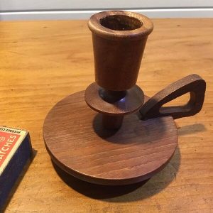 Vintage wooden candle holder with a drip tray and finger loop handle beside a vintage matchbox for scale, on a timber table