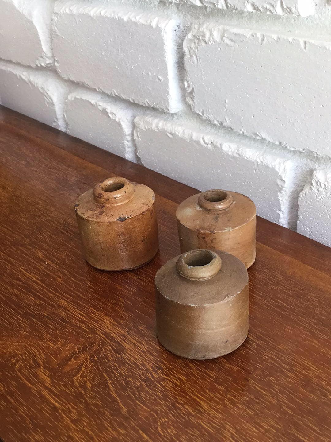 Three salt glazed stoneware inkwells on a timber sideboard, showing the glaze wear and small chips